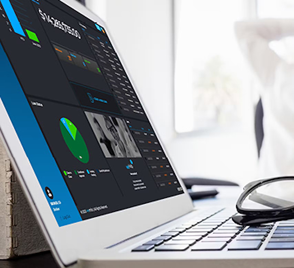 A close-up of a laptop displaying colorful data charts and dashboards. In the background, an out-of-focus person stretches with arms behind their head, and eyeglasses rest next to the laptop. A close-up of a laptop displaying colorful data charts and dashboards. In the background, an out-of-focus person stretches with arms behind their head, and eyeglasses rest next to the laptop.